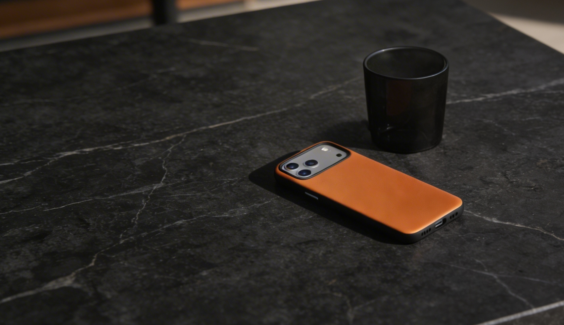 A smartphone with a Crazy Horse leather case rests on a dark marble table next to a black cup.